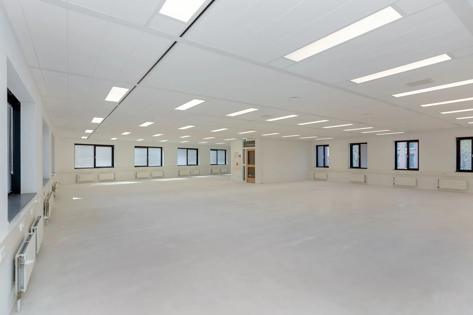 Lichte, lege kantoorruimte aan de Boris Pasternaklaan met witte muren, ramen rondom en systeemplafondverlichting.